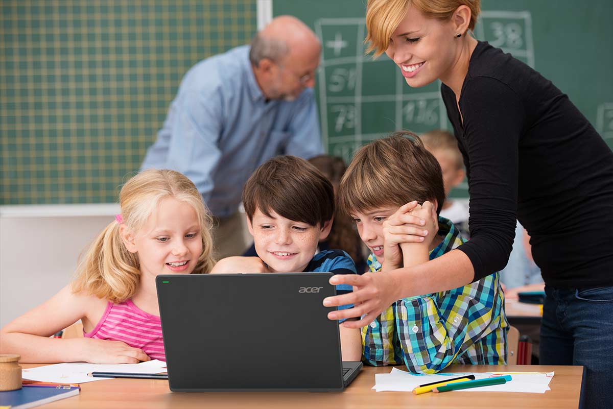 Docente sorridente con bambini studenti felici guardando un notebook